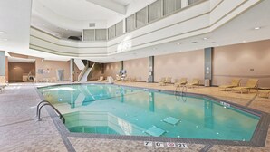 Une grande piscine intérieure d’une profondeur de 2,13 mètres, entourée de chaises longues et dotée d’un escalier menant à un niveau supérieur.