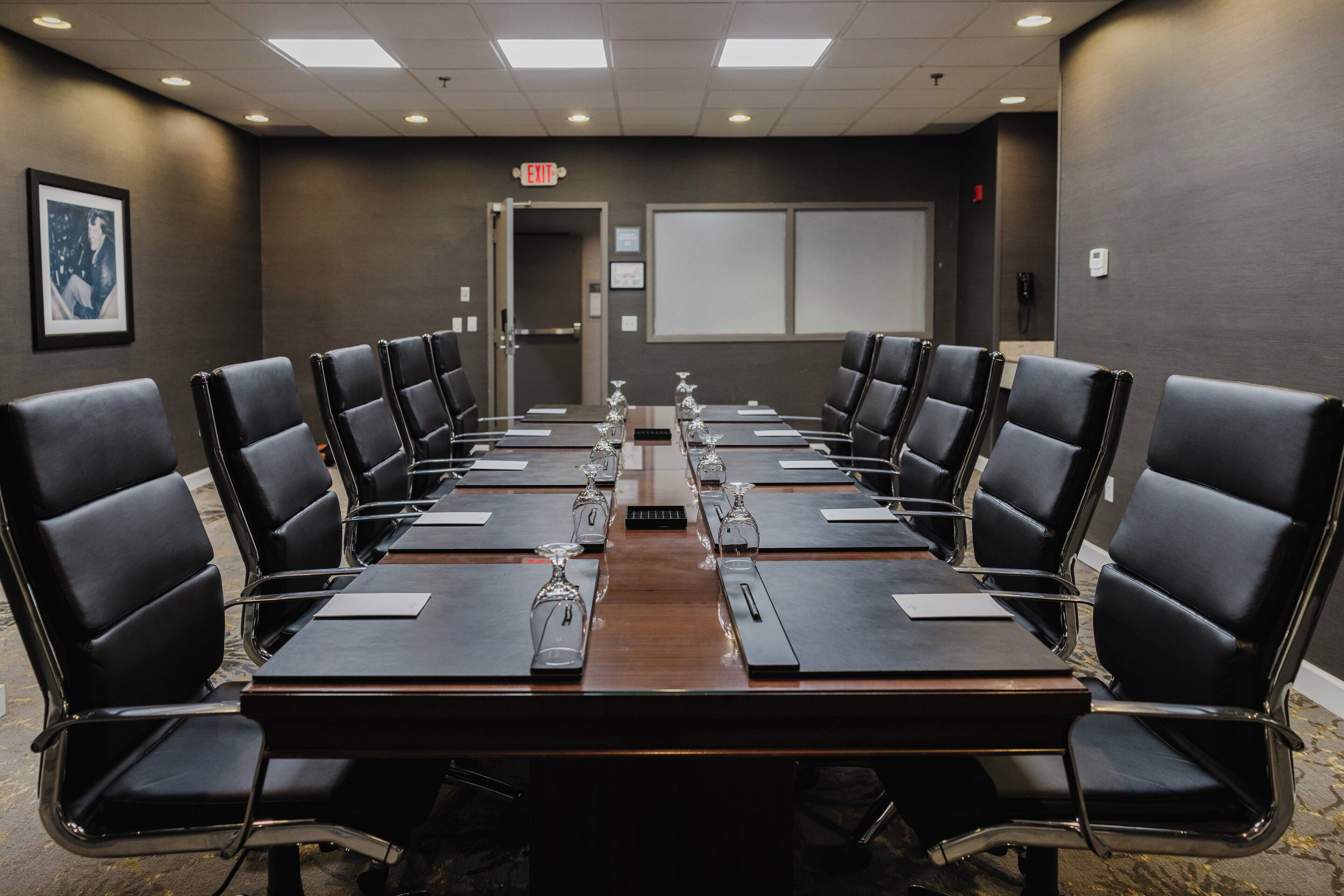 A conference room with a long table, black leather chairs, and a projector screen on the wall.