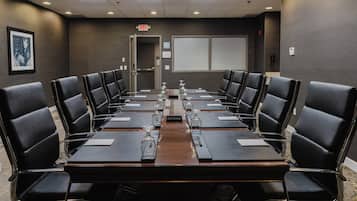 A conference room with a long table, black leather chairs, and a projector screen on the wall.