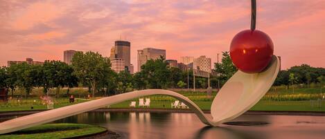 A park with a unique sculpture, a body of water, and a city skyline in the background.