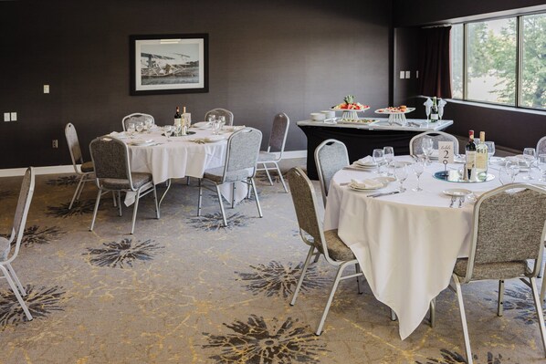 Un comedor con mesas dispuestas para una comida, sillas, una mesa de buffet con alimentos y una ventana con vistas.