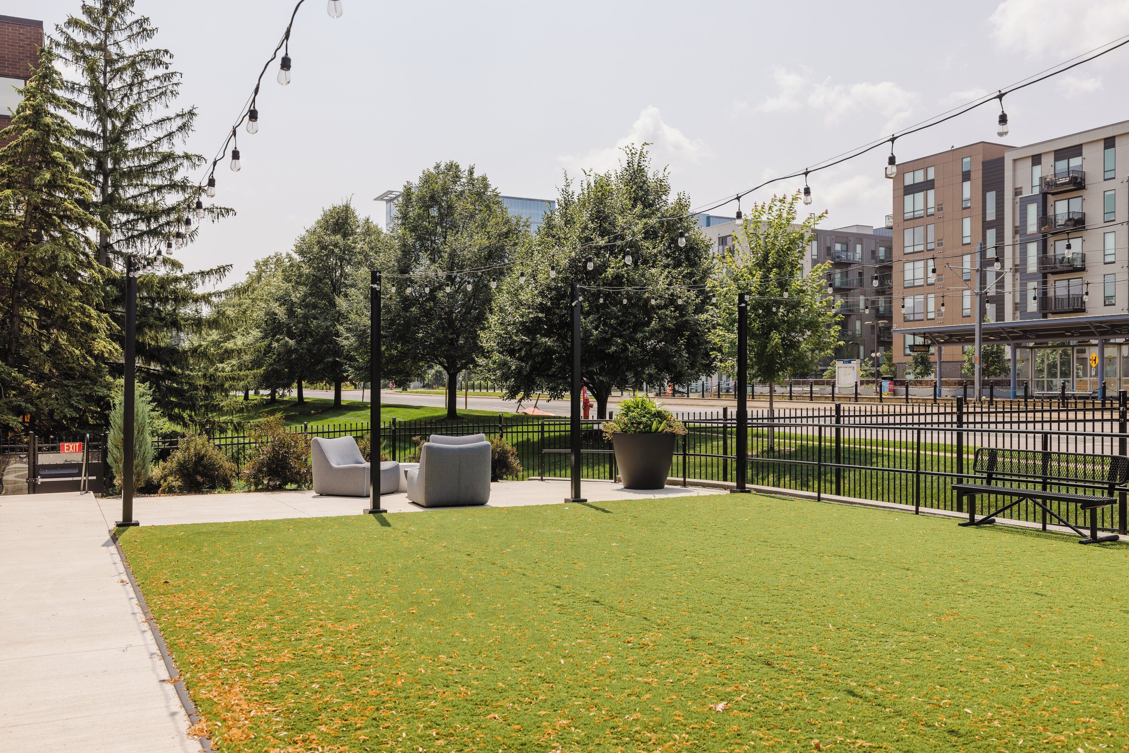 A park with grass, trees, benches, and a fence.