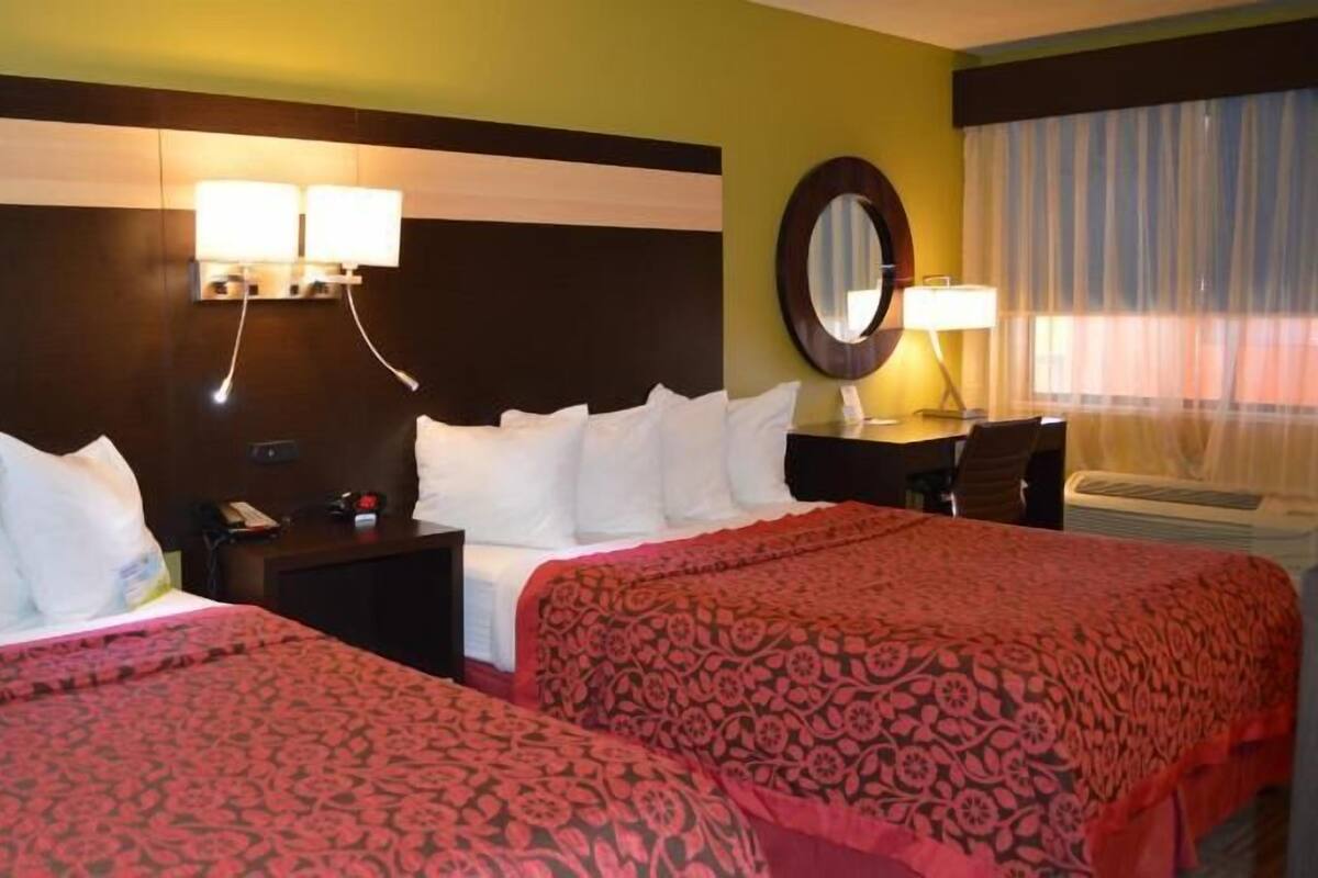 A hotel room with two beds, a desk, a chair, a mirror, and a window with curtains.