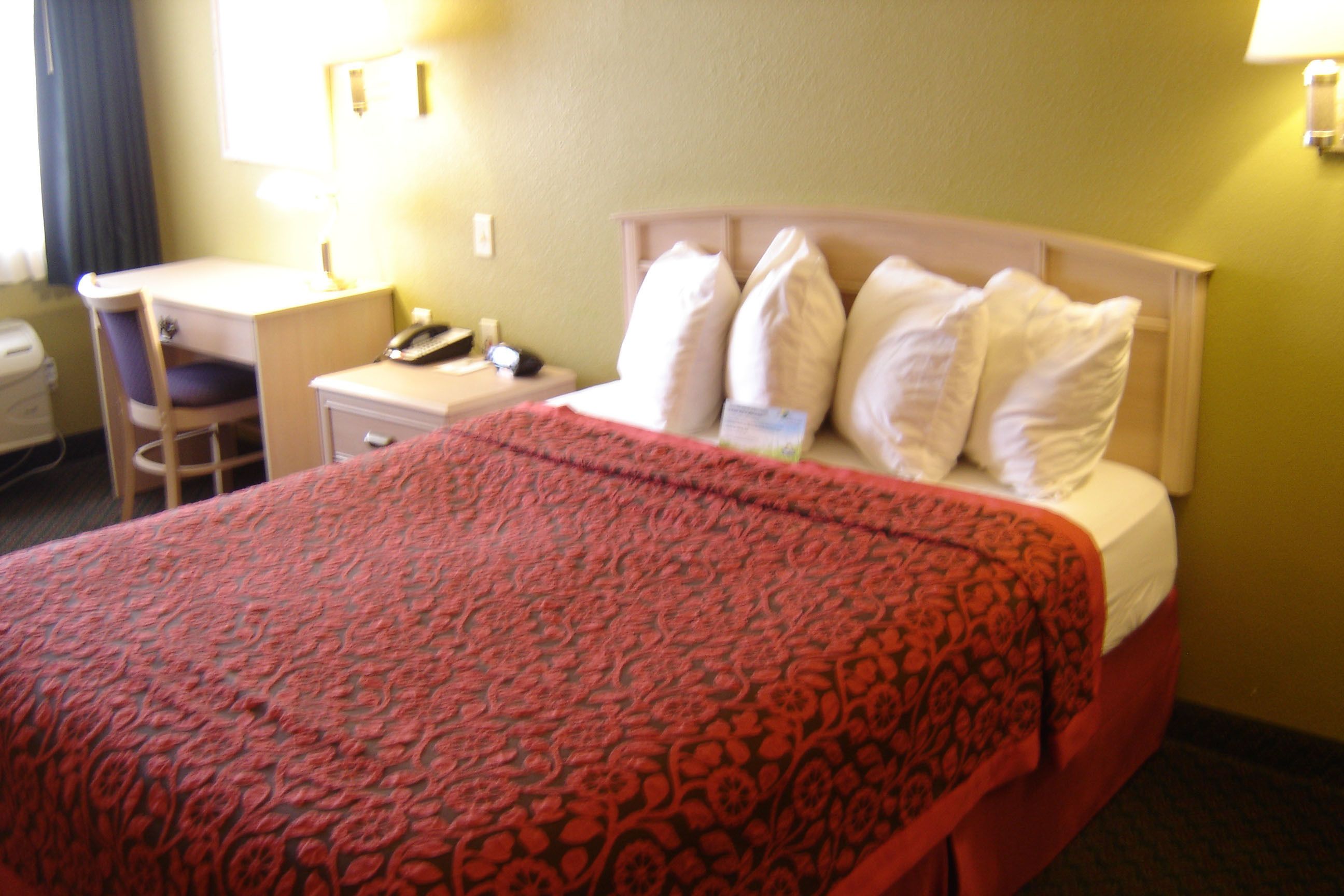 A hotel room with a bed, a desk, a chair, and a nightstand.