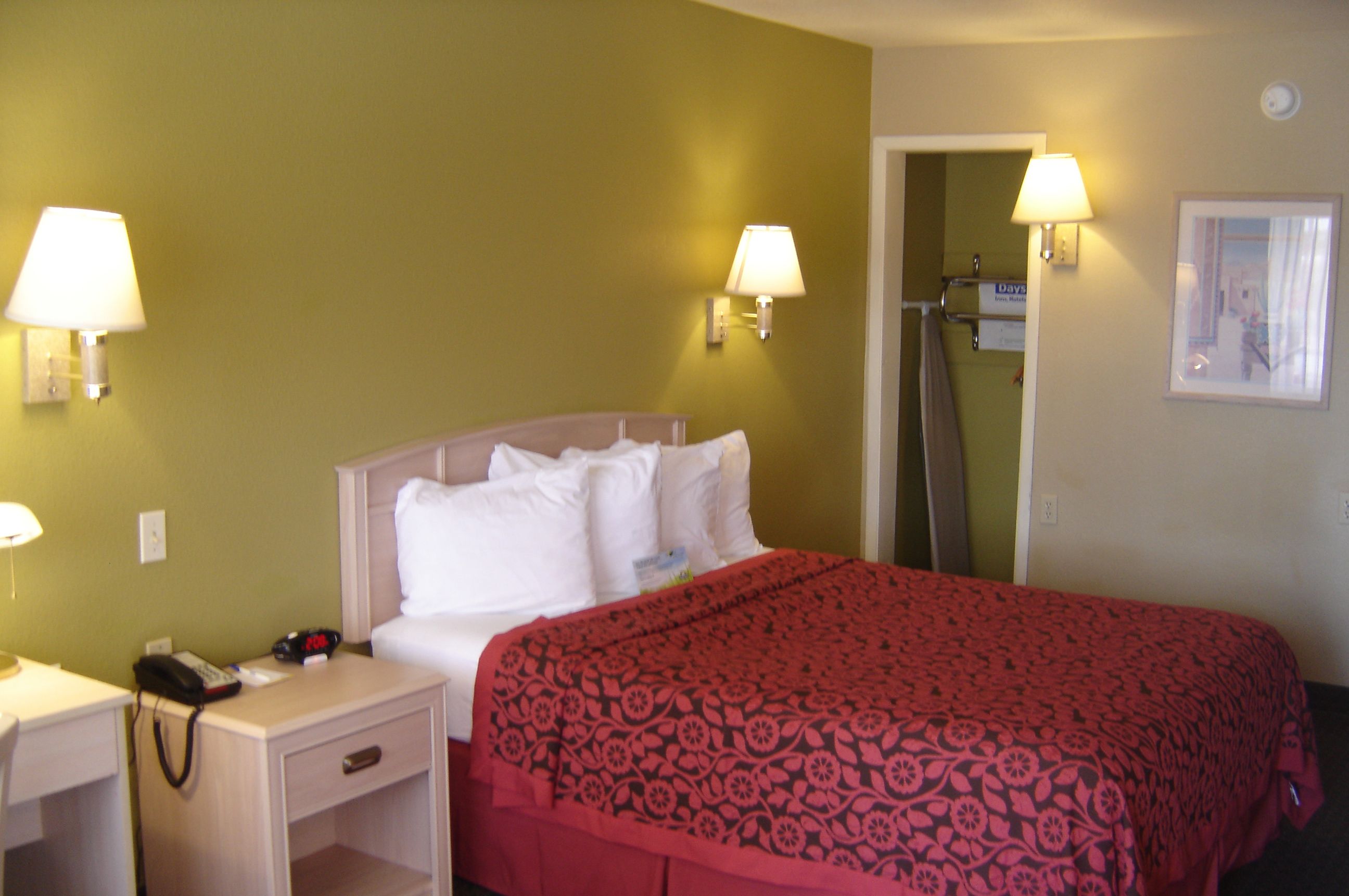 A hotel room with a bed, bedside lamps, a nightstand, and a door leading to a bathroom.