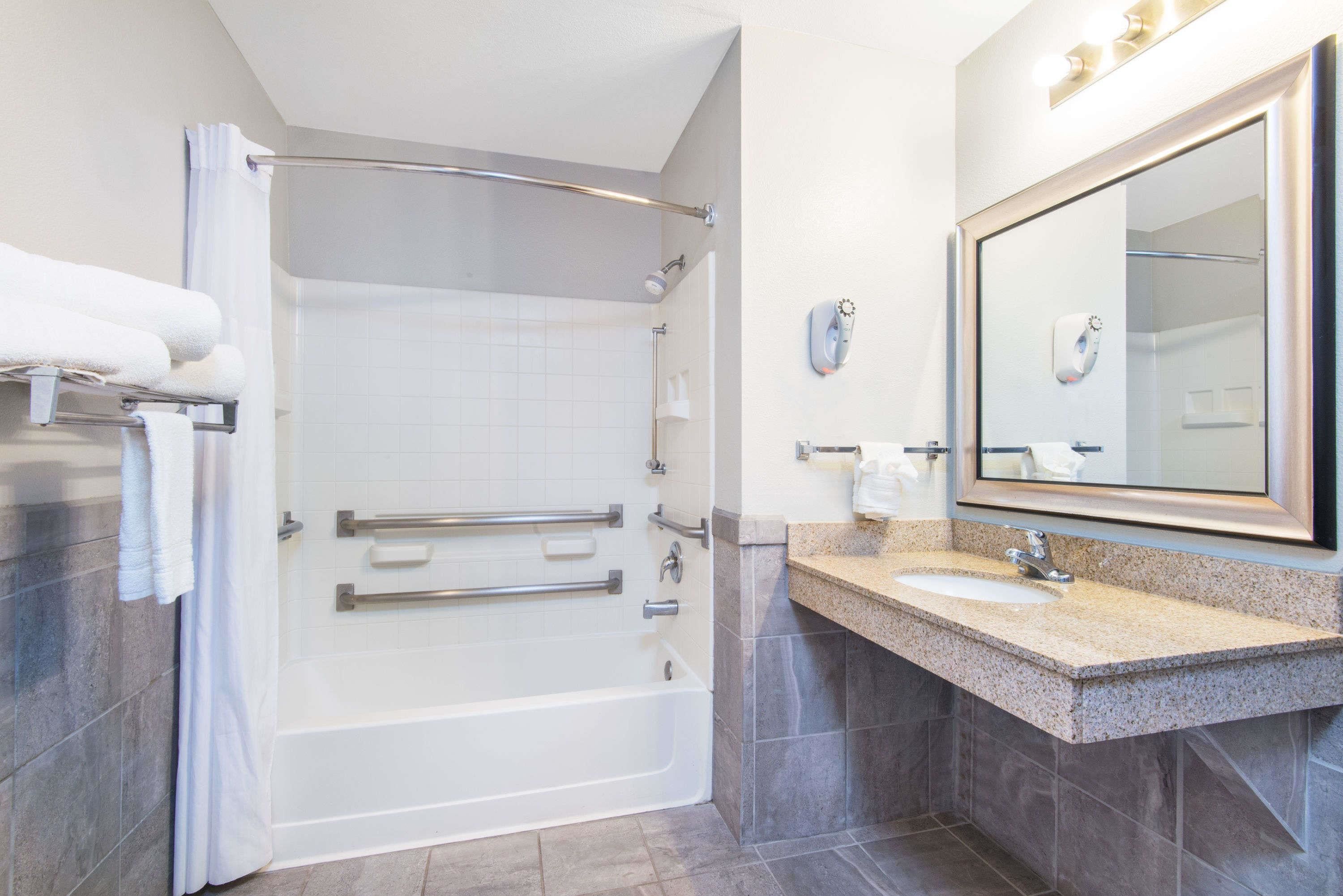 A modern bathroom with a walk-in shower, grab bars, a sink with a vanity, and a large mirror.