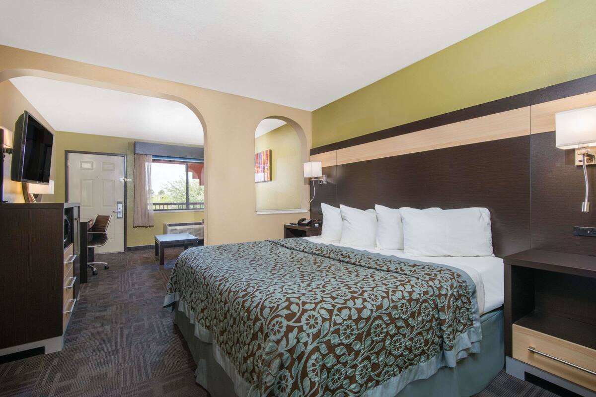 A hotel room with a large bed, a desk, a chair, a TV, and a window.