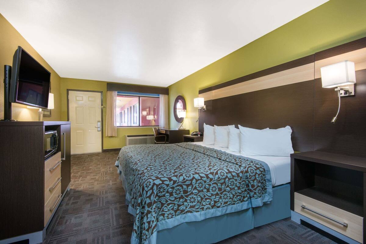 A hotel room with a bed, a desk, a television, and a window.