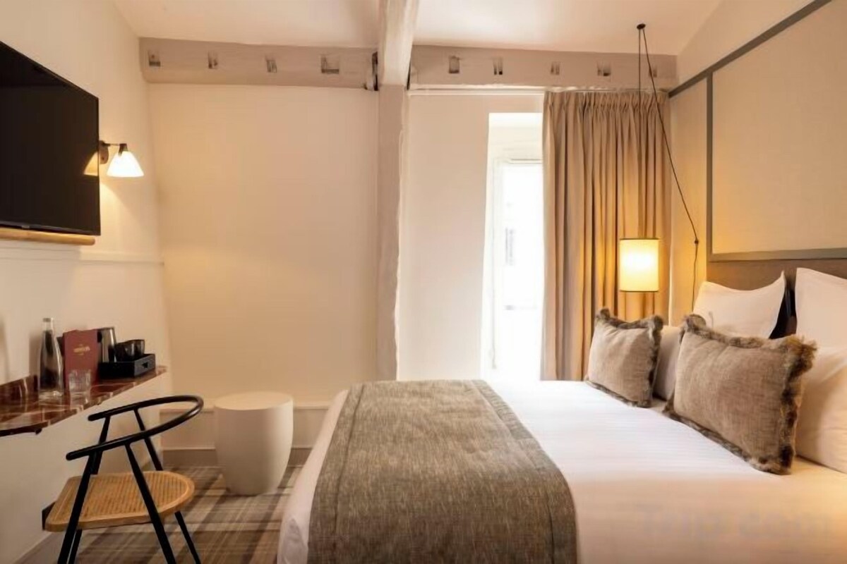 Ein Hotelzimmer mit einem Bett, einem Schreibtisch mit Stuhl, einem Fernseher und einem Fenster mit Vorhängen.
