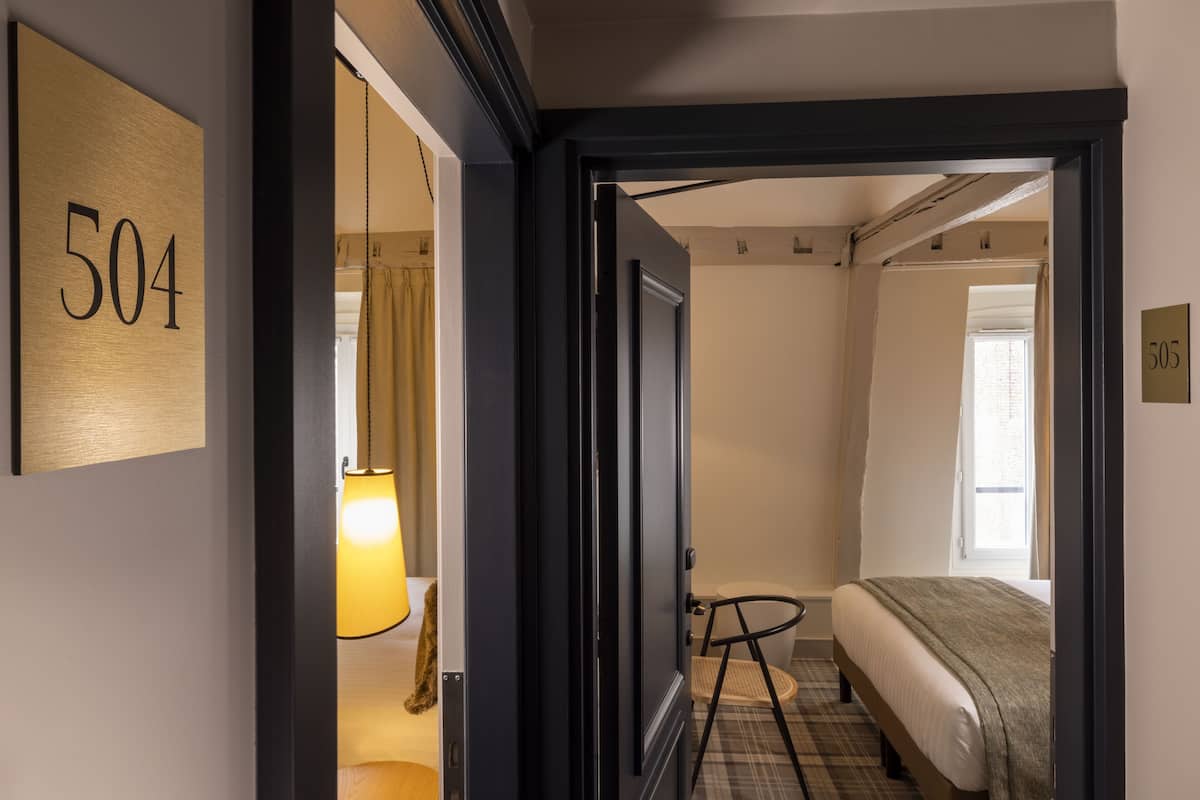 Ett hotellrum med en säng, en stol, en lampa och en dörr som leder till ett annat rum.