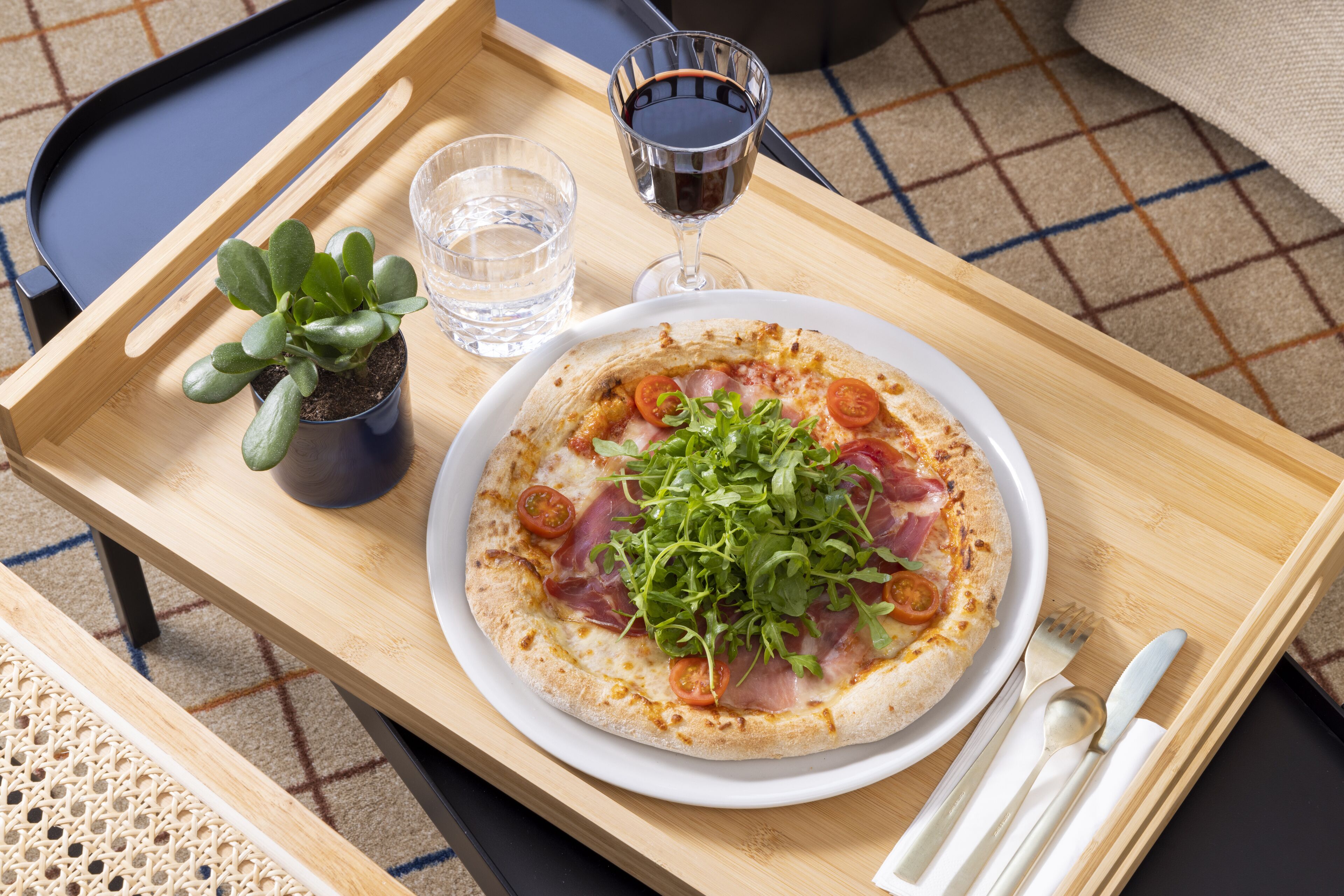 A wooden tray with a pizza, a glass of water, and a glass of red wine.