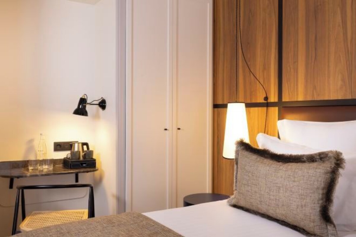 A hotel room with a bed, a bedside table with a lamp, a chair, and a wooden panel wall.