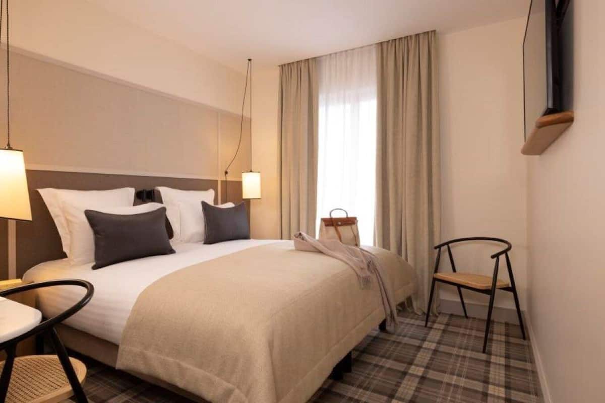 Ett hotellrum med en säng, en stol, ett bord och en tv som är monterad på väggen.