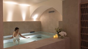 A spa room with a large bathtub, a small table with candles, and a decorative vase with flowers. - Hôtel Toujours & Spa (Paris)