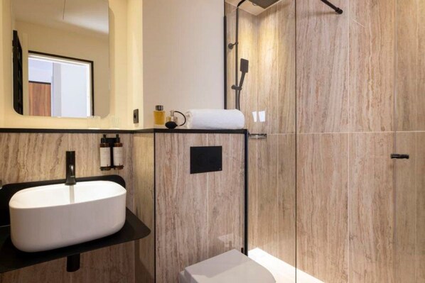 Un baño moderno con un lavamanos grande blanco, un espejo, una ducha con cabezal de ducha de mano y un inodoro.