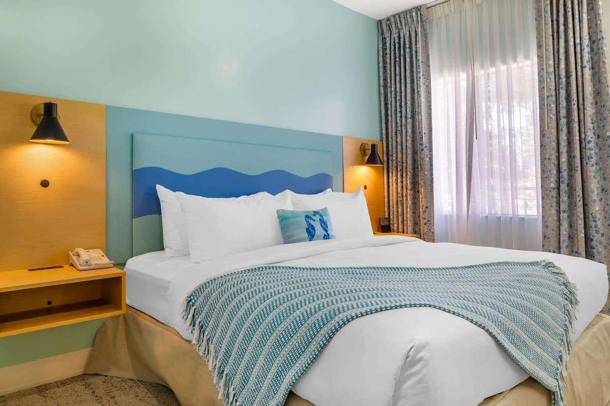 A hotel room with a bed, a nightstand with a phone, and a wall-mounted lamp.