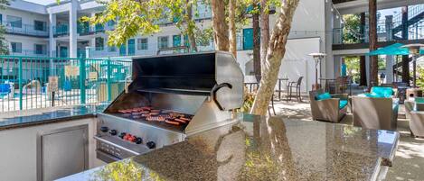 An outdoor barbecue area with a grill, seating, and a view of the building in the background.