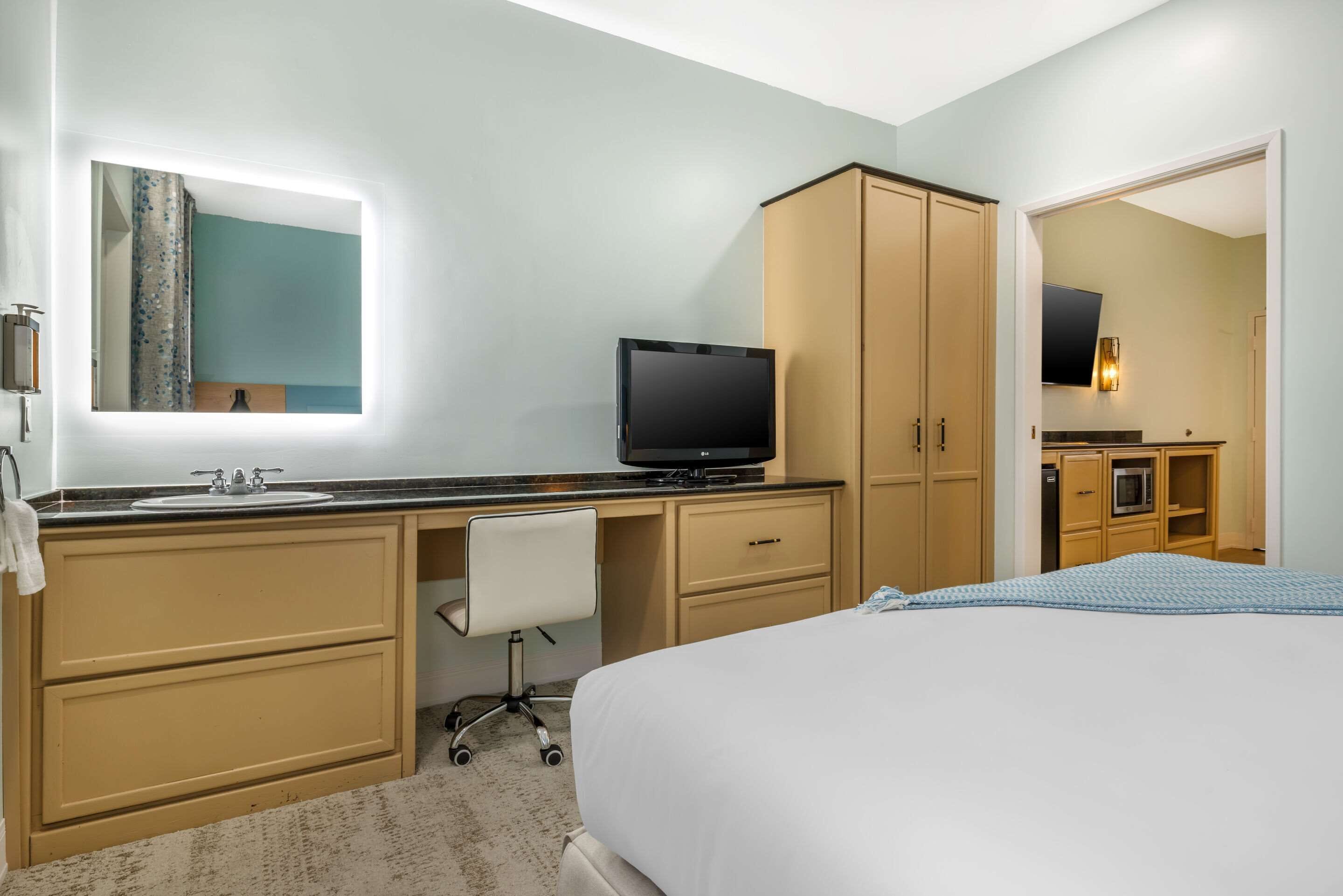 Una habitación de hotel con cama, escritorio con silla, televisor, espejo y armario.