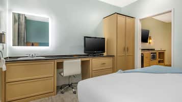 Una habitación de hotel con cama, escritorio con silla, televisor, espejo y armario.