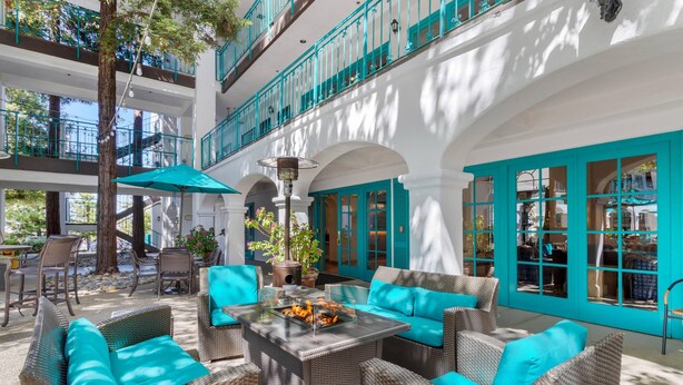 Un vaste espace extérieur aménagé avec des meubles en osier et des coussins turquoise, offrant une vue sur un bâtiment blanc agrémenté de touches bleu-vert.