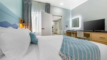 A hotel room with a bed, a desk, a TV, and a bathroom visible through an open door.