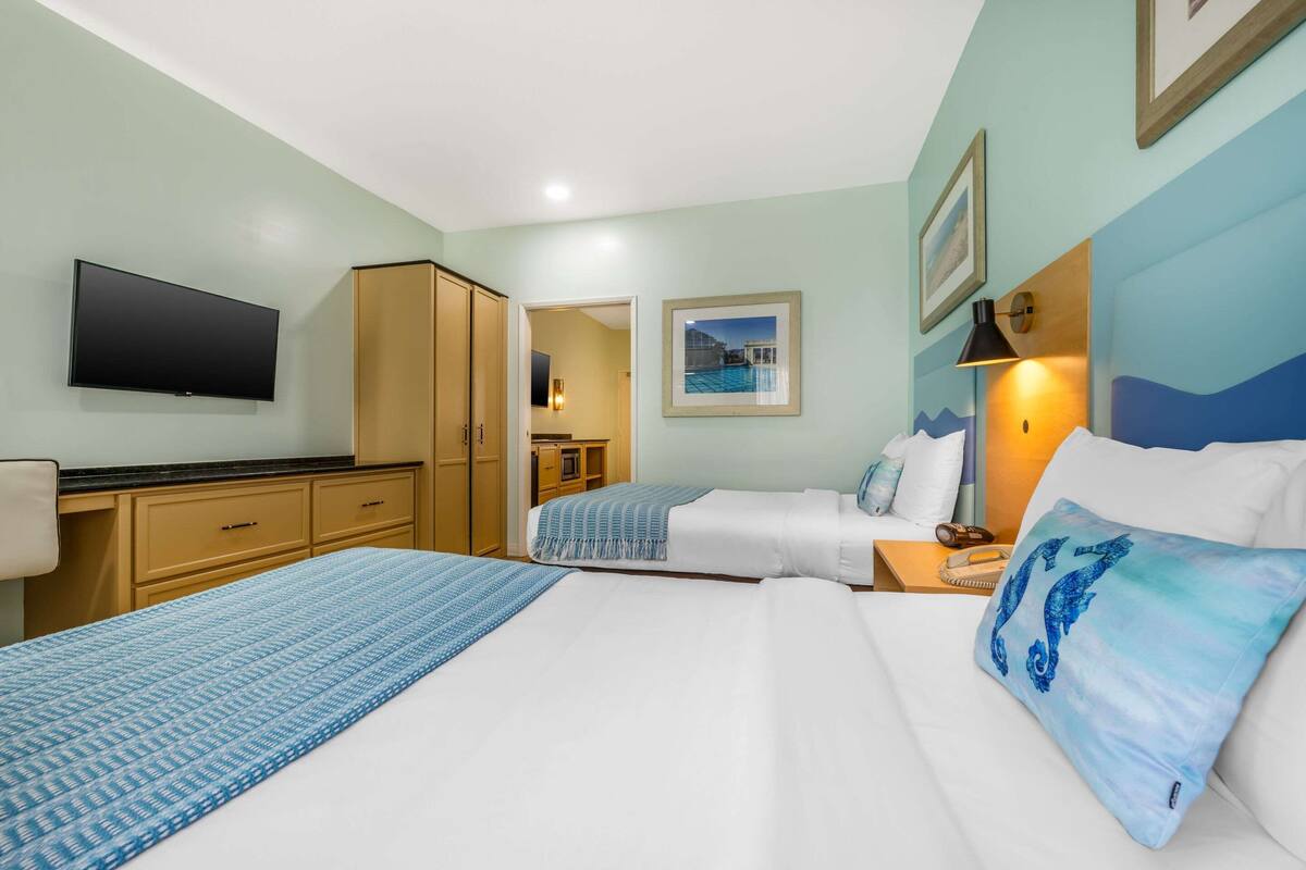 A hotel room with two beds, a TV, wooden cabinets, a desk, and a framed picture on the wall.