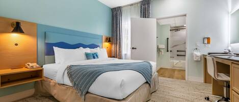 Quarto de hotel com cama, mesas de cabeceira, escrivaninha e banheiro visível por uma porta aberta.