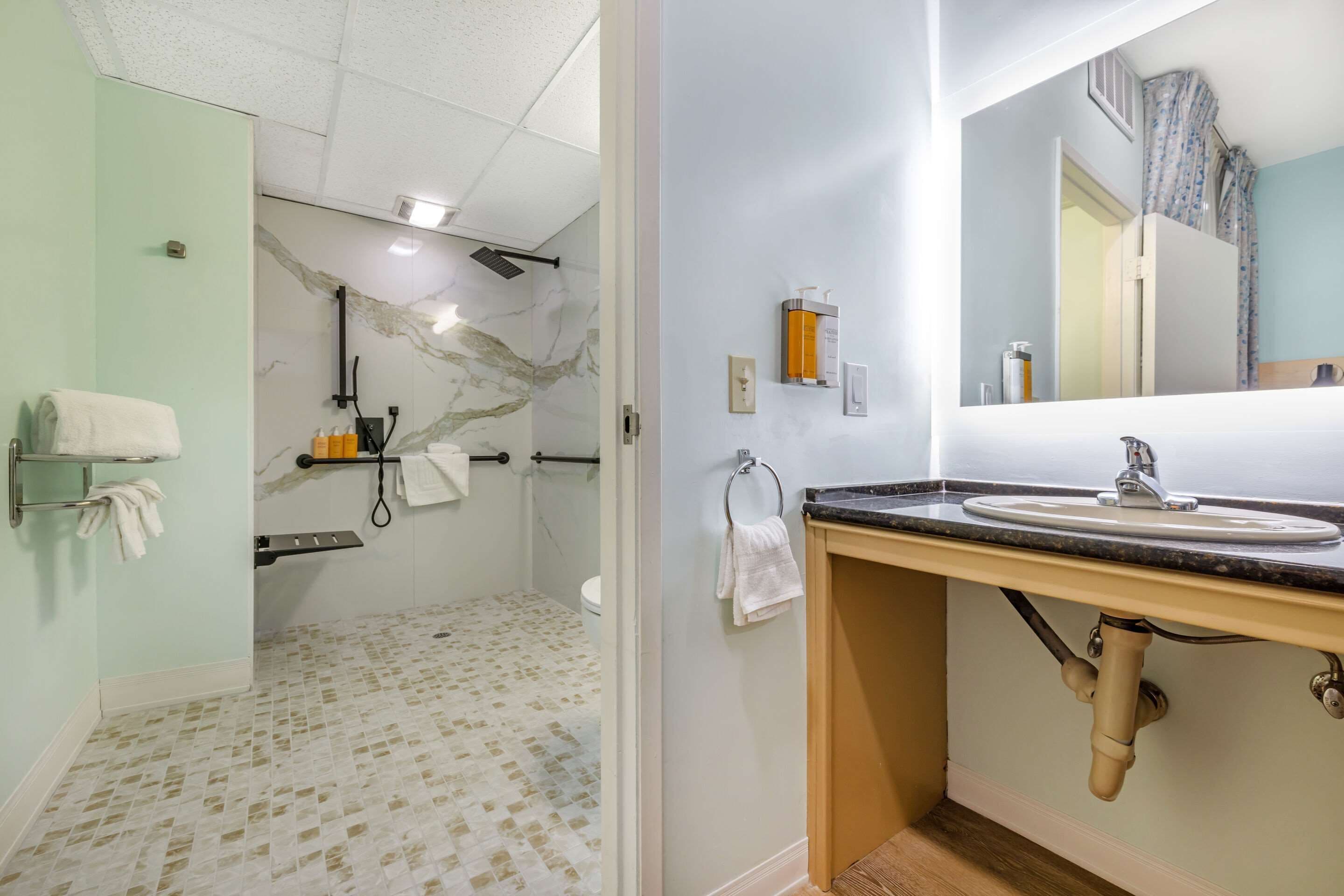 A bathroom with a marble shower wall, a sink with a vanity, and a towel rack.