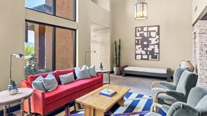 Un amplio salón con un sofá rojo, una mesa de centro de madera, un sillón gris, un tapete estampado y una planta de cactus.