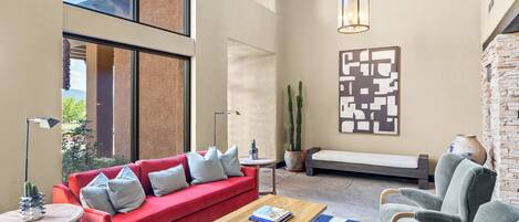 Un vaste espace de vie comprenant un canapé rouge, une table basse en bois, un fauteuil gris, un tapis à motifs et un cactus.