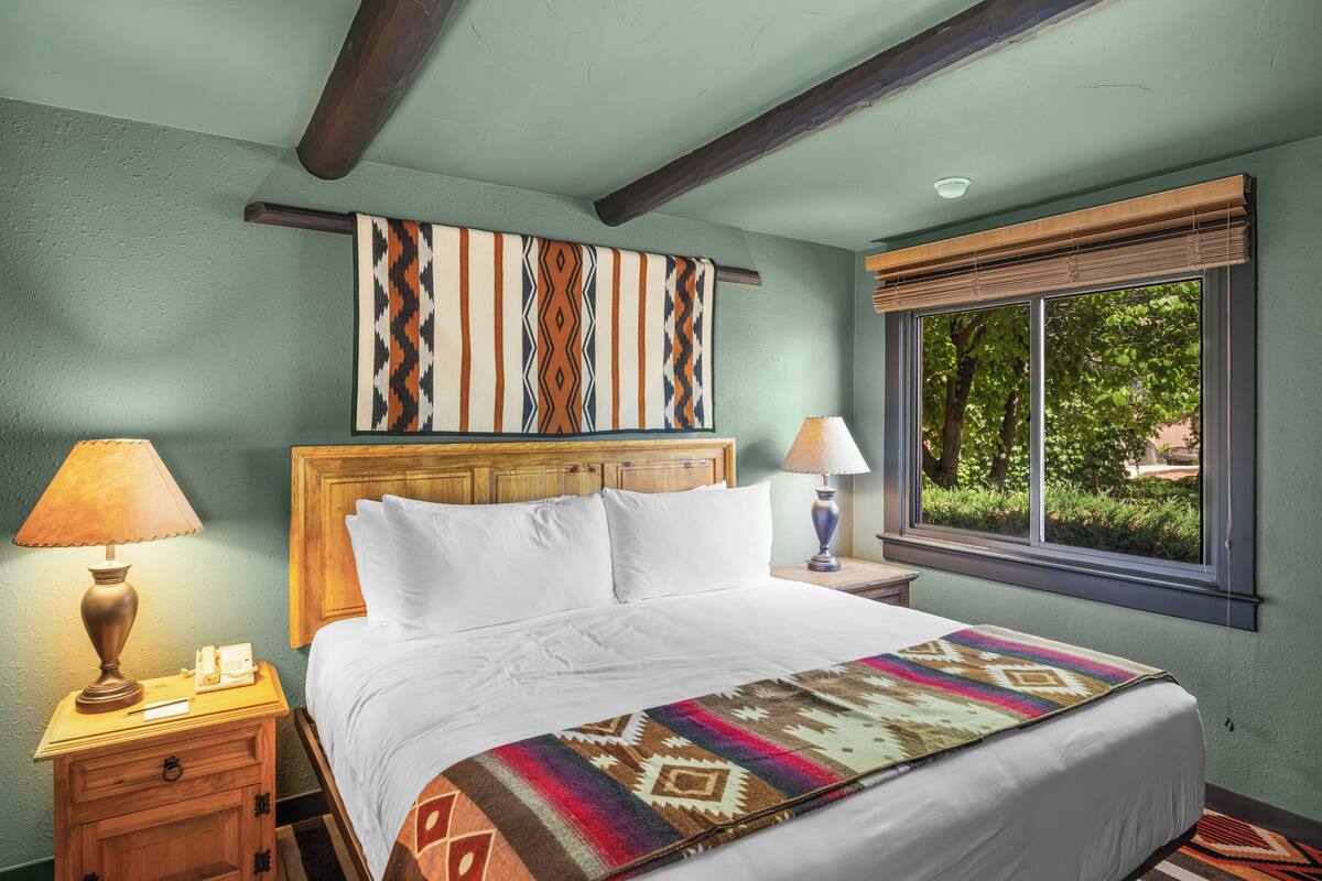 Un lit bien fait, avec une couverture à motifs, une tête de lit en bois et une fenêtre donnant sur un paysage verdoyant.
