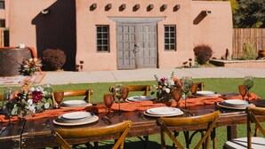 Un área de comedor al aire libre con una mesa dispuesta para una comida, sillas y un centro de mesa decorativo.