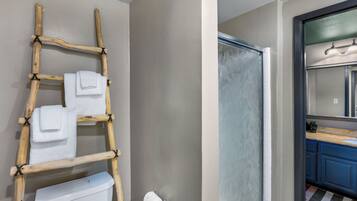 A bathroom with a wooden ladder holding towels, a toilet paper holder, and a shower with a frosted glass door.