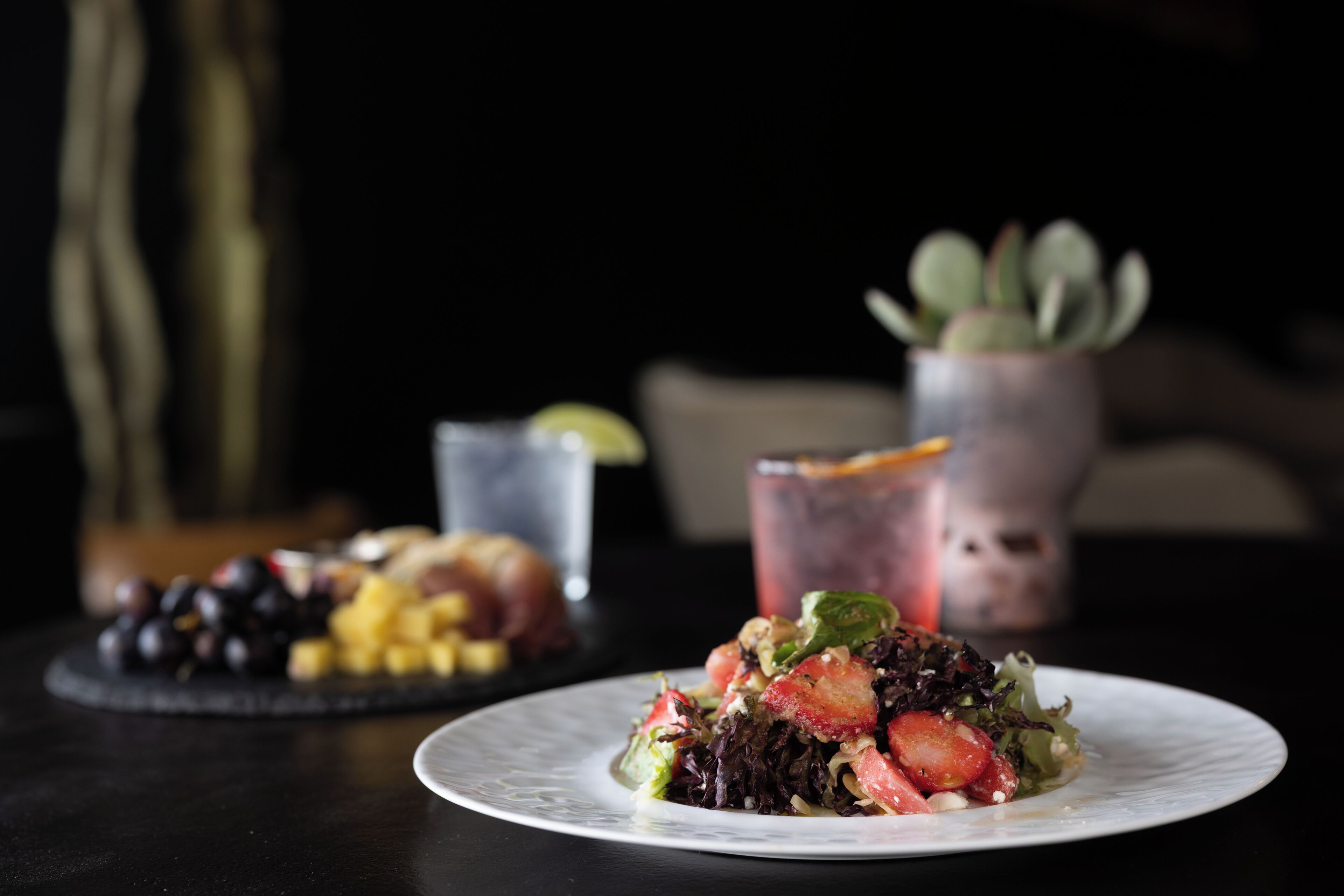 A plate of food with a salad and fruit on a table, a glass of drink, and a potted plant in the background.