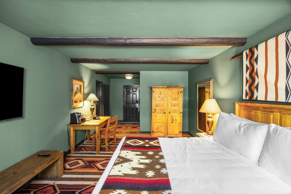 Une chambre d’hôtel comprenant un lit, un bureau avec une chaise, une armoire en bois et un téléviseur fixé au mur.
