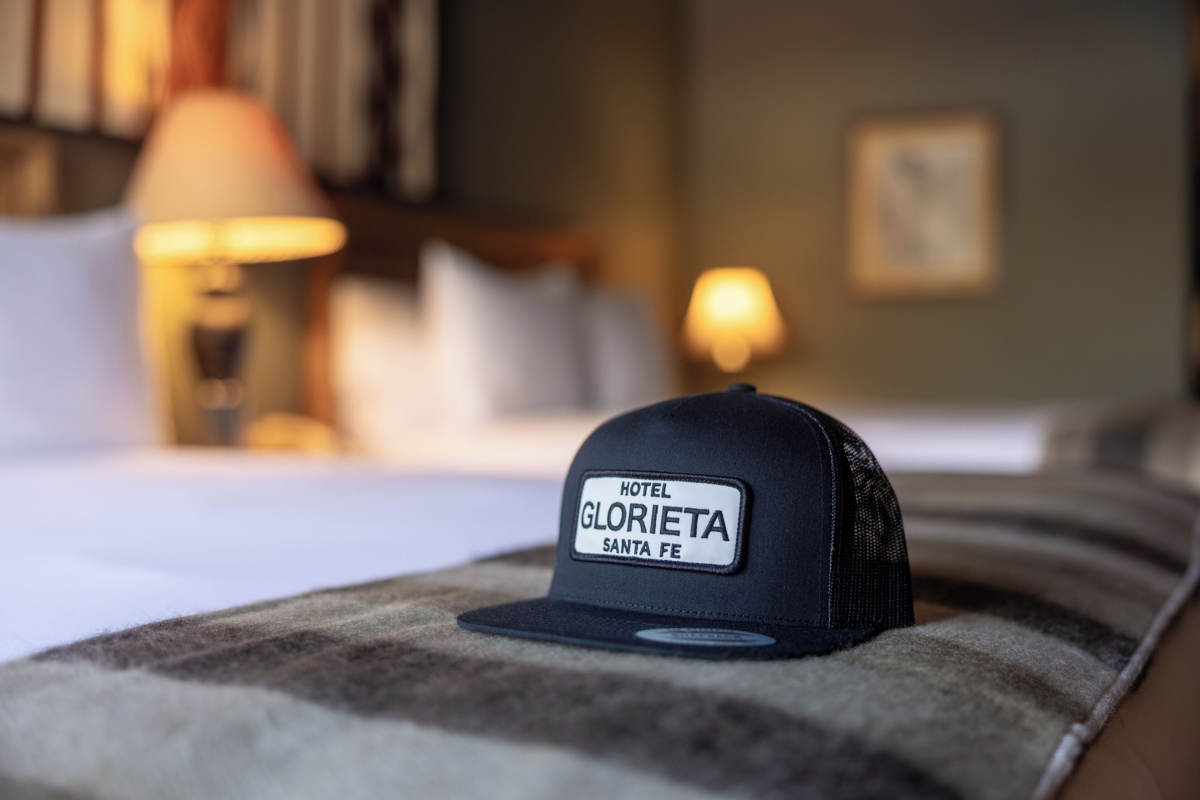 A black cap with a label that reads 'HOTEL GLORIETA SANTA FE' placed on a bed.