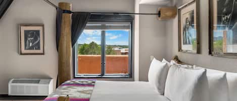 A hotel room with a bed, a window with a view, and a wall-mounted air conditioner.