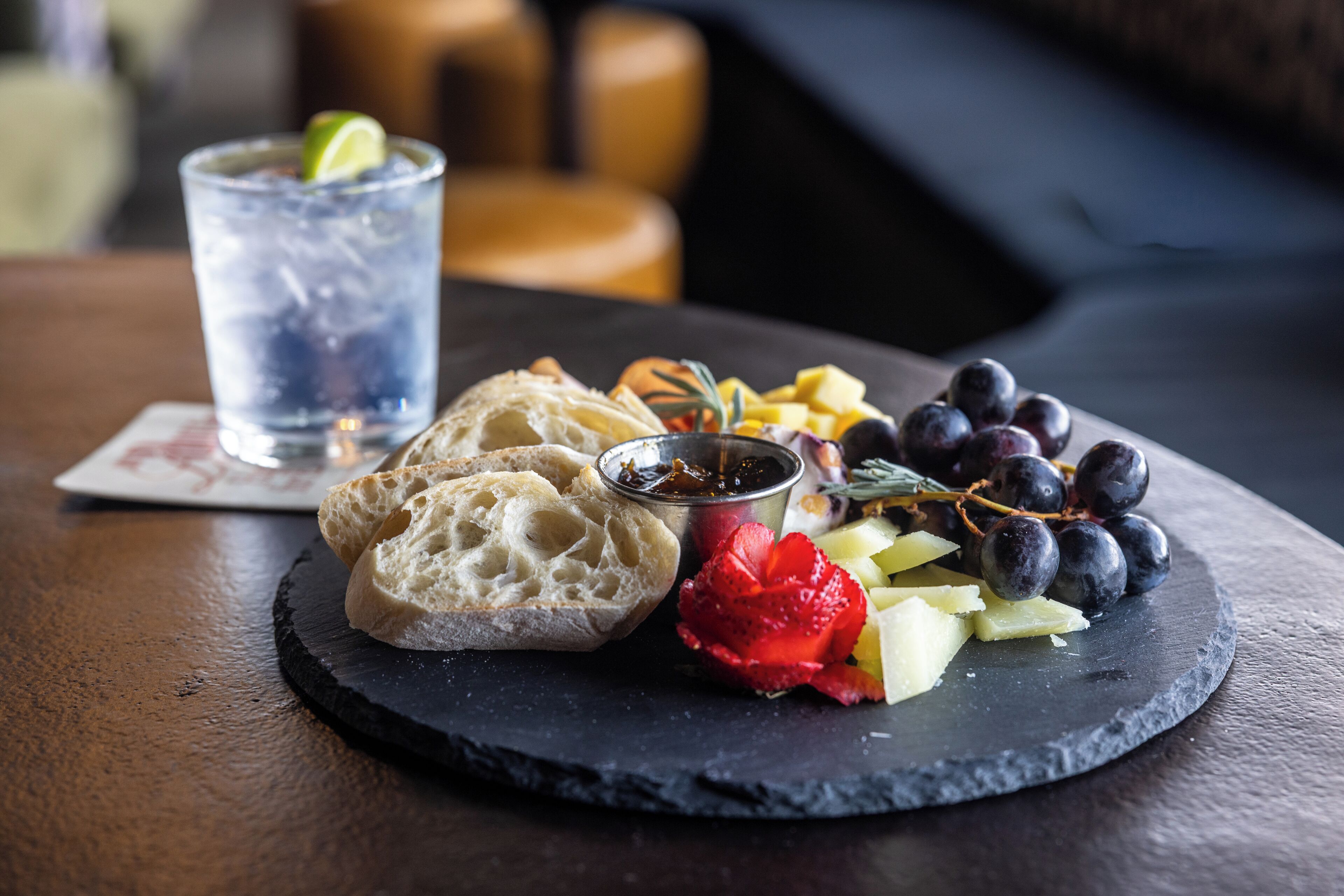 Una pizarra con pan, uvas, fresas y una bebida sobre una mesa de madera.