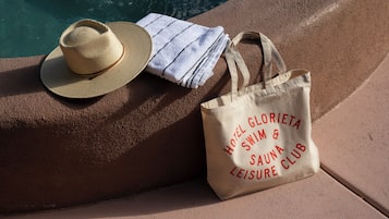 A straw hat, a striped towel, and a tote bag with text on a poolside surface.
