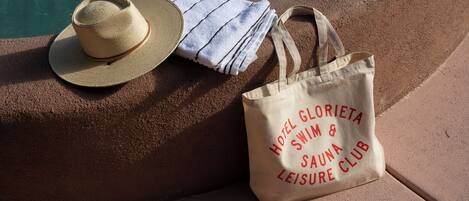 Un chapeau de paille, une serviette à rayures et un sac fourre-tout avec un motif imprimé, le tout posé sur une surface au bord de la piscine.