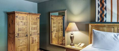 A hotel room with a large wooden wardrobe, a bedside table with a lamp, and a bed with white linens.