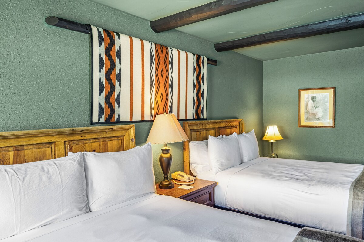 A hotel room with two beds, a wooden headboard, a wall-mounted artwork, and a framed picture.