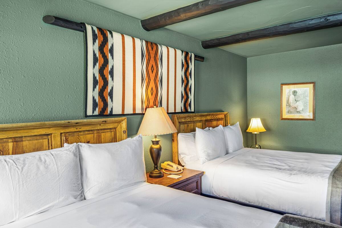 Une chambre d’hôtel avec deux lits, une tête de lit en bois, une œuvre d’art accrochée au mur et un tableau encadré.