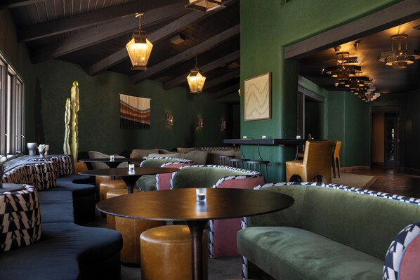 A modern lounge area with green walls, patterned sofas, and wooden tables.