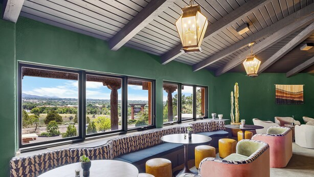 Un interior acogedor con vistas al paisaje, que incluye una zona de estar con mesas redondas y sillas acolchadas, vigas de madera en el techo y una pared verde.