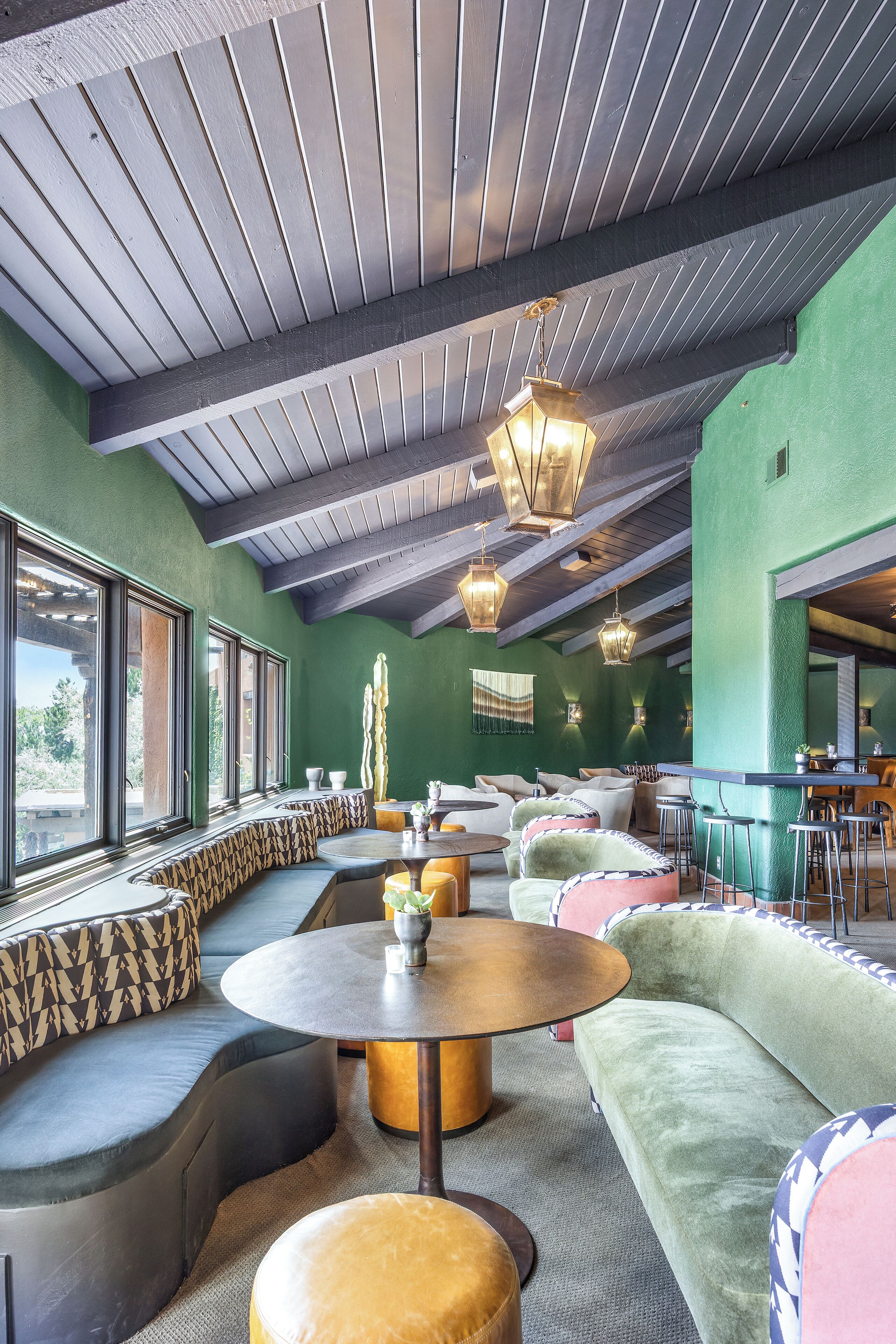 A modern interior with a green wall, wooden ceiling beams, and a seating area with cushioned sofas and a round table.