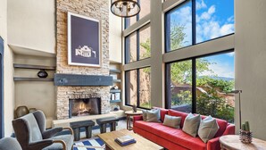 Una sala de estar moderna con chimenea de piedra, sofá rojo y ventanas grandes que ofrecen vistas al exterior.
