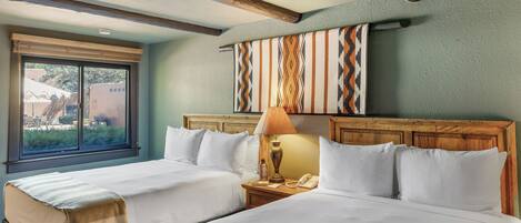 A hotel room with two beds, a window with a view, a wooden headboard, and a wall-mounted lamp.
