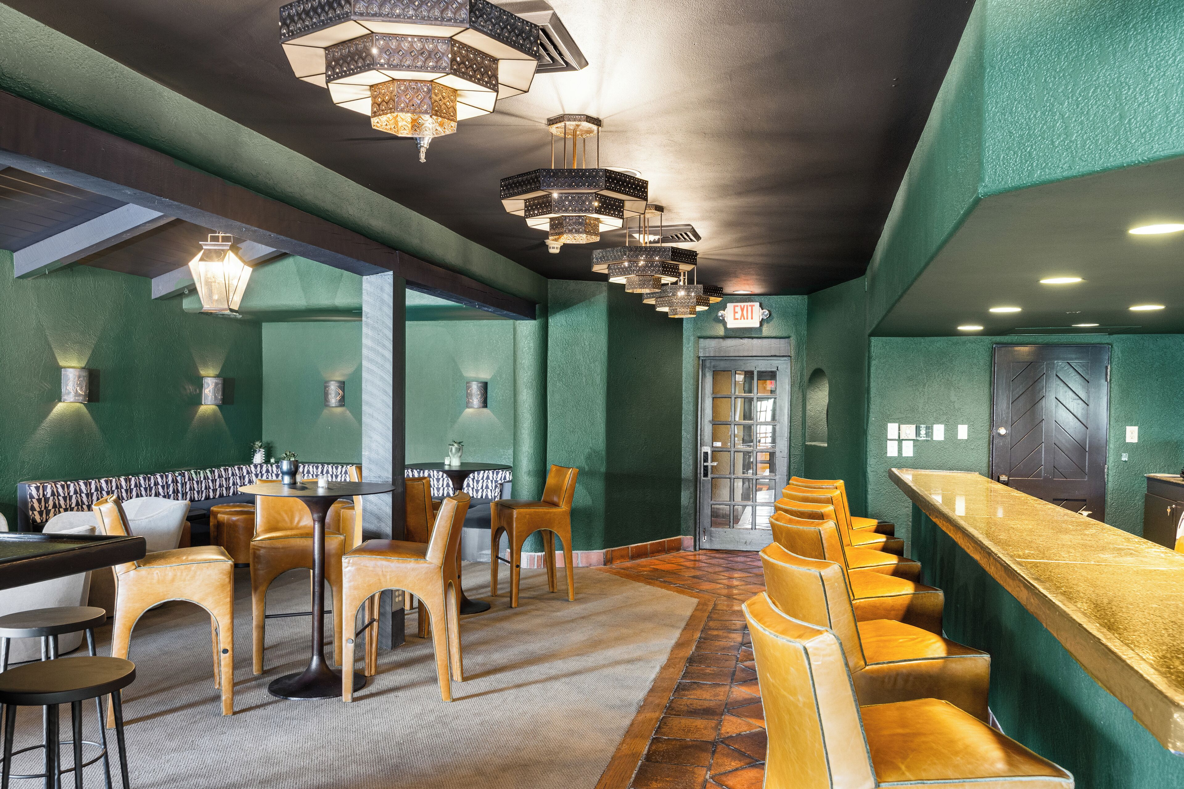 A bar area with a long counter and multiple stools. There are tables and chairs arranged in the foreground.