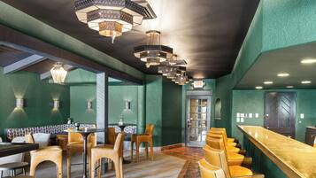 A bar area with a long counter and multiple stools. There are tables and chairs arranged in the foreground.